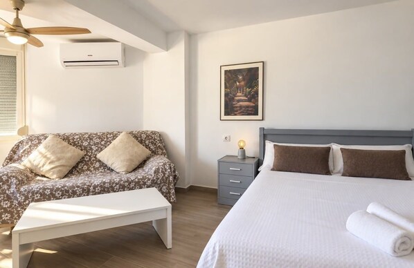 Un dormitorio con cama, sofá, mesita de noche y aire acondicionado de pared.