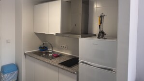 Eine kleine Küche mit Spüle aus Edelstahl, einem eingebauten Backofen und einem kompakten Kühlschrank.