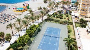 A tennis court surrounded by palm trees and a beach with a colorful water slide. - Loft in 1st Line Residential with pool (Algarrobo Costa)