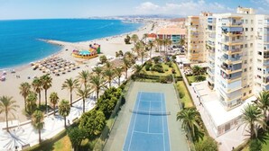 A coastal area with a beach, palm trees, a tennis court, and residential buildings. - Loft in 1st Line Residential with pool (Algarrobo Costa)