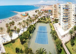 Eine Küstenlandschaft mit Strand, Palmen, einem Tennisplatz und Wohnhäusern.