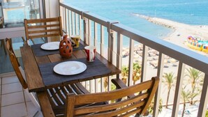 A balcony with a table set for two, overlooking a beach with people and umbrellas. - Loft in 1st Line Residential with pool (Algarrobo Costa)