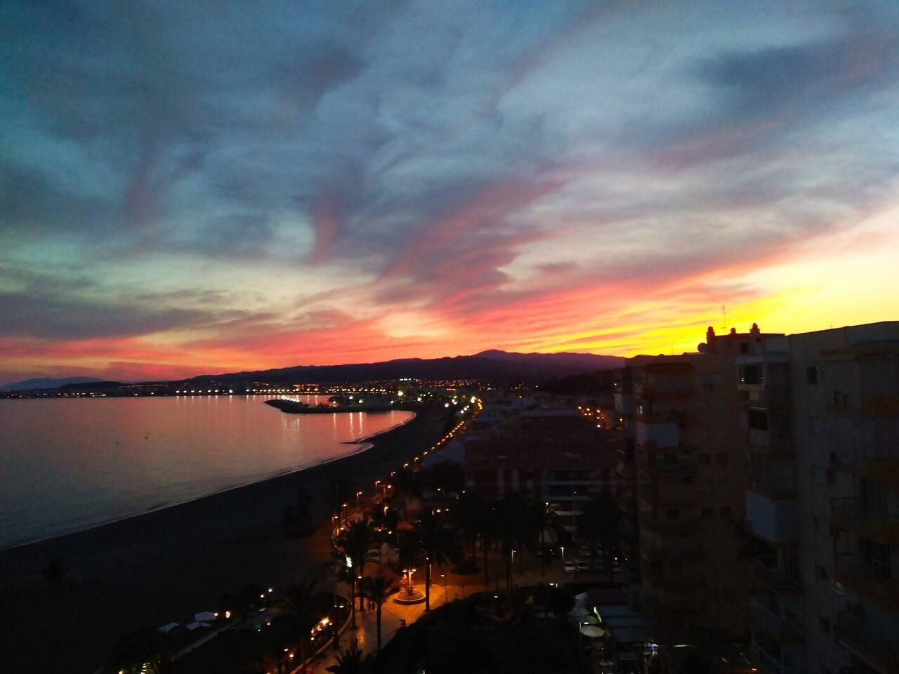 Paesaggio costiero al crepuscolo con un ponte e edifici lungo il lungomare.
