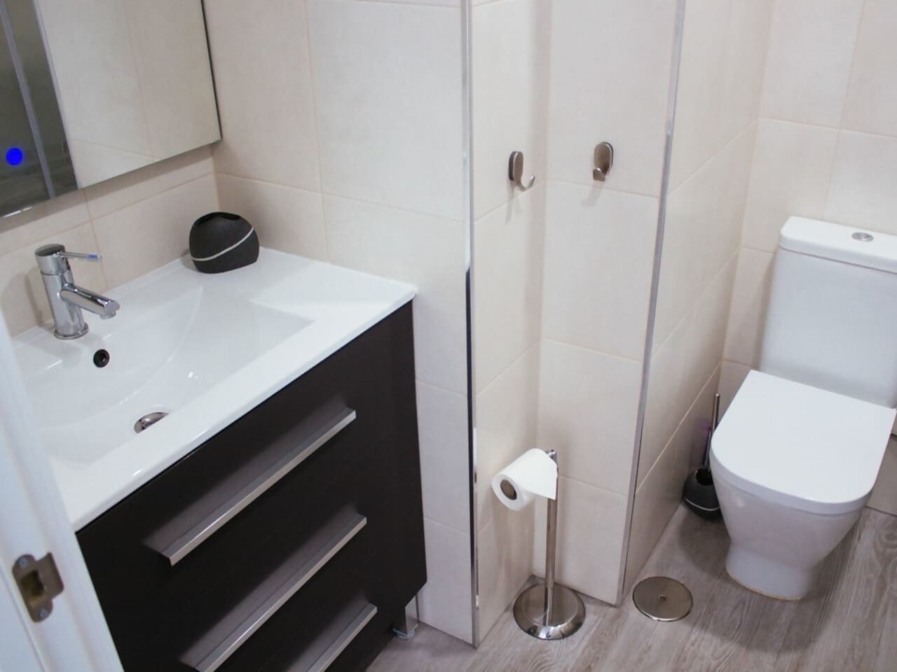 Et moderne badeværelse med hvid vask, mørk skabssektion, toilet og en lille skraldespand.