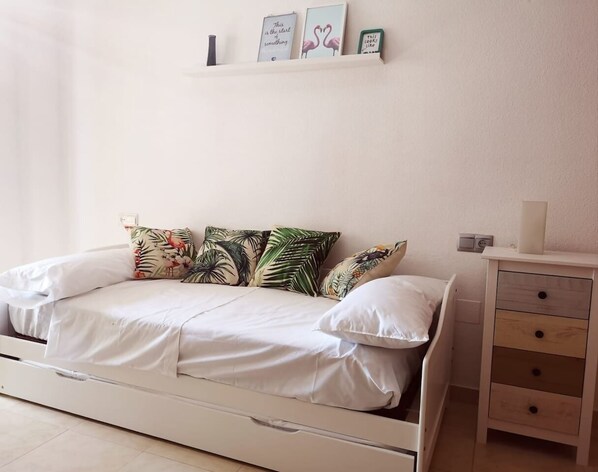 A bedroom with a bed, pillows, a nightstand, and a shelf with framed pictures.