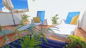 Una terraza en la azotea con dos tumbonas, una mesita y plantas en macetas.