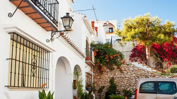 Una calle estrecha con edificios blancos, muros de piedra y plantas en macetas.