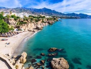 Un pueblo costero con playa, costa rocosa y montañas al fondo.