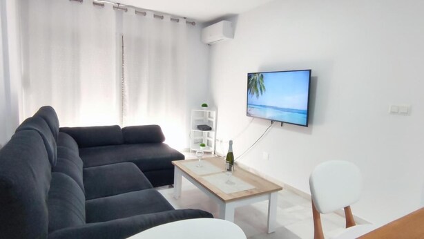 A modern living room with a dark-colored sofa, a white coffee table with a bottle and glass, and a flat-screen TV on the wall. - FANTASTIC FULLY RENOVATED APARTMENT (Torre Del Mar)