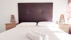 A neatly made bed with white linens and two rolled towels in front. There are two bedside tables with lamps on either side of the bed. - FANTASTIC FULLY RENOVATED APARTMENT (Torre Del Mar)