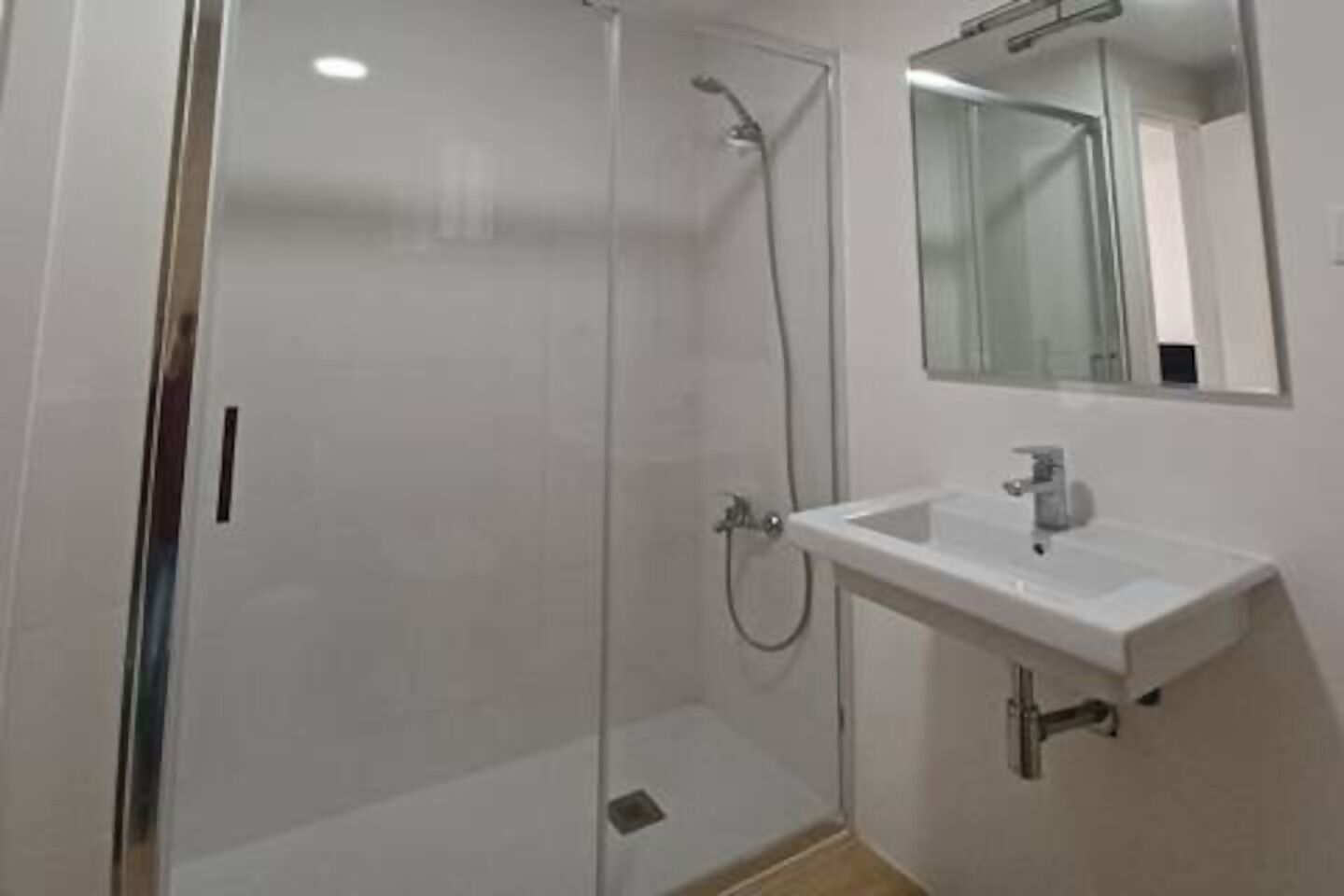 A bathroom with a glass shower enclosure, a white sink, and a mirror above the sink.