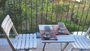 Un patio con dos sillas de metal blanco y una mesa dispuesta con tazas y una cuchara.