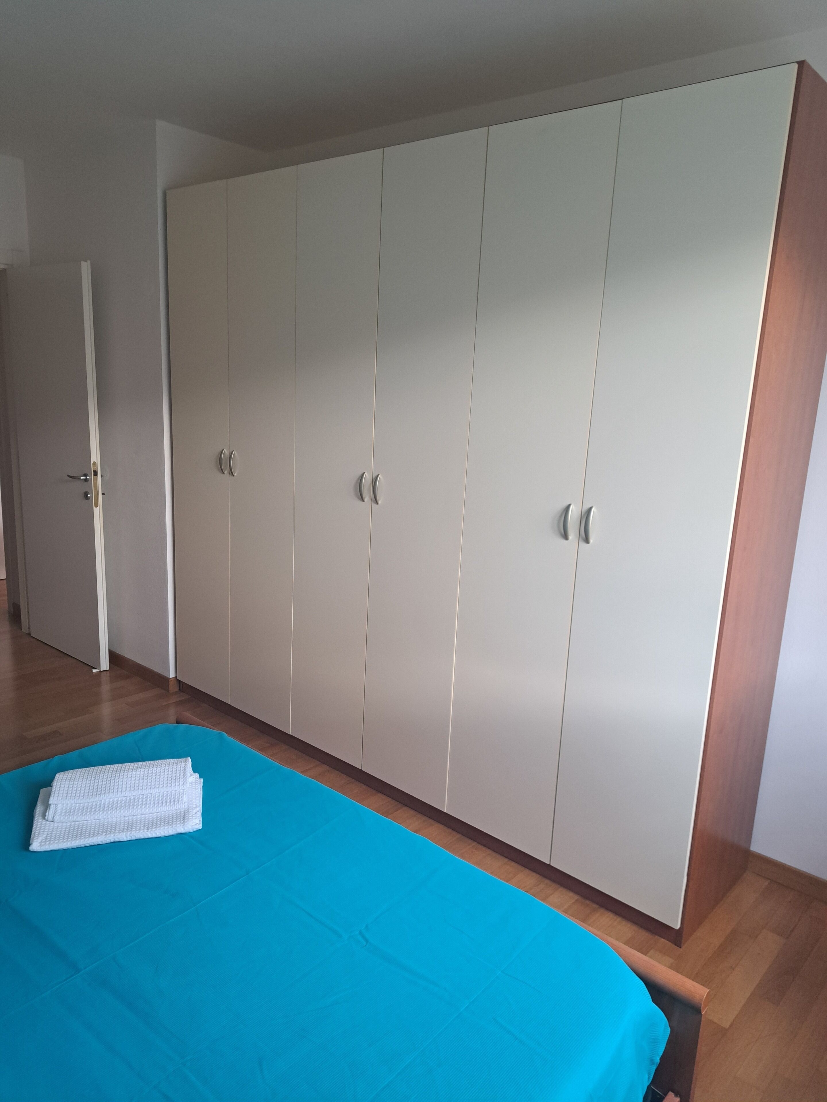 Un dormitorio con un armario grande, una cama con colcha azul y suelo de madera.