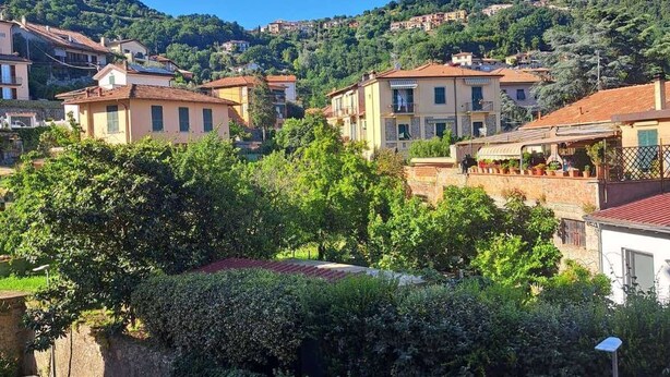 Una zona residencial en una ladera, con casas, una calle con coches aparcados y abundante vegetación.