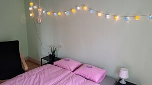 Un dormitorio con cama, una silla, una mesita con lámpara y luces decorativas.