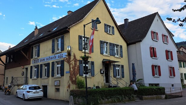 Un edificio con un letrero que dice "BAR zum scharfe egg" y una bandera suiza.