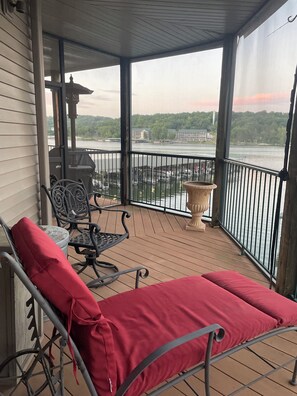 Une terrasse extérieure couverte avec vue sur une rivière, un barbecue et un espace salon avec des coussins rouges.