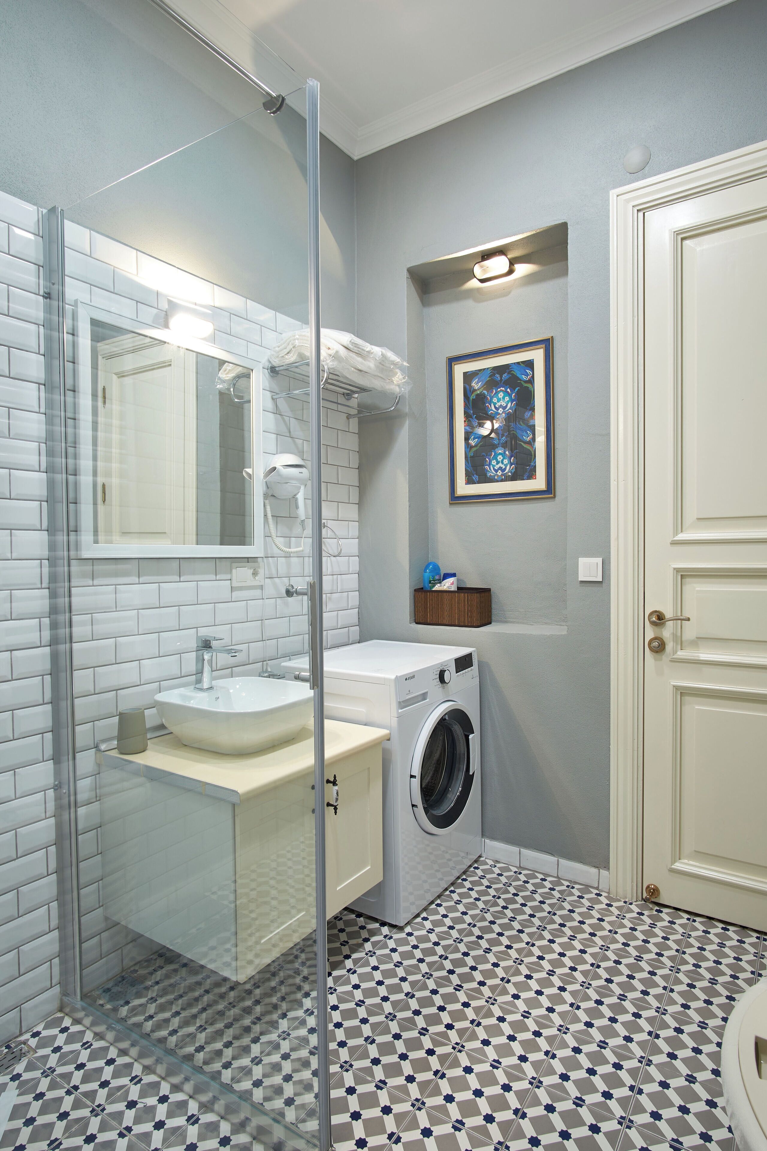 A bathroom with a glass shower enclosure, a sink, a washing machine, and a door.