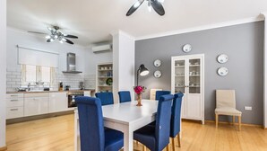 Une cuisine moderne avec des meubles blancs, une table à manger entourée de chaises bleues et un mur d’accent de couleur grise.