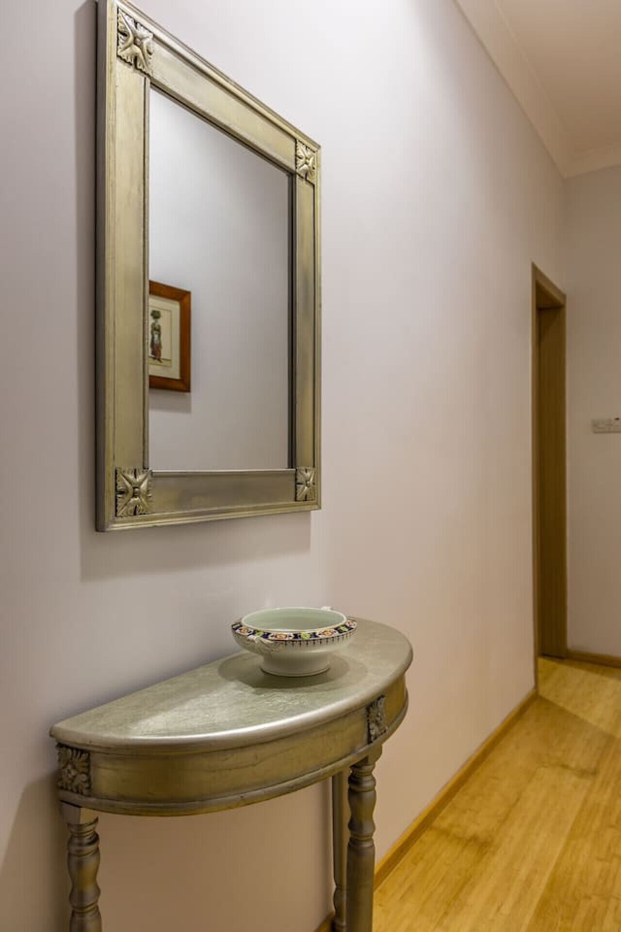 A hallway with a mirror on the wall and a small table with a bowl on it.