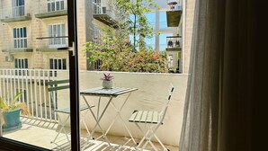 Un balcon avec une table et des chaises, un pot de fleurs et une vue sur les bâtiments voisins.