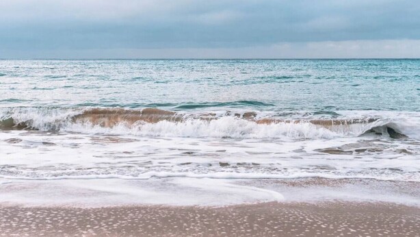 Une plage où les vagues se brisent sur le rivage sous un ciel nuageux.