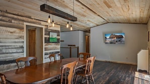 A dining area with a wooden table and chairs, a wooden ceiling, and a painting on the wall.