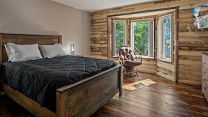A bedroom with a wooden bed, a chair, and large windows.