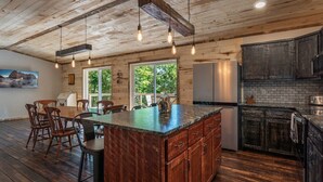 A rustic kitchen with wooden beams, a large island, and a view of greenery outside.