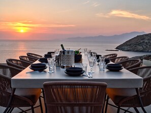 A table set for dining with a view of the sea and mountains during sunset.