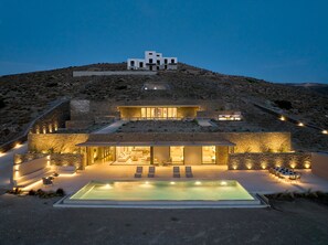 A modern villa with a swimming pool, outdoor seating, and a view of the surrounding landscape.