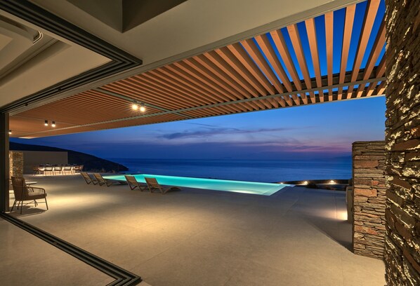 An outdoor pool area with lounge chairs and a view of the ocean at dusk.