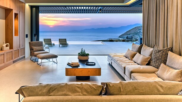 Un salon moderne doté d’une grande fenêtre donnant sur la mer, d’un canapé, de fauteuils et d’une table basse.