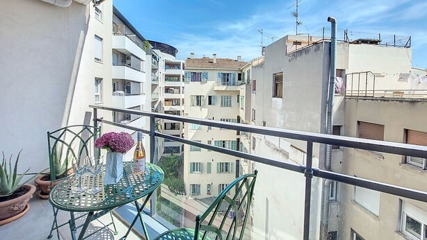 A balcony with a glass table, chairs, potted plants, and a bottle of wine. - N&J - VAGUE AZUR - Central - Balcony (Niza)