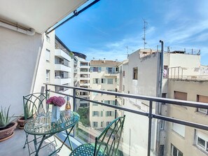 Ein Balkon mit Glastisch, Stühlen, Topfpflanzen und einer Weinflasche.