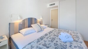 A neatly made bed with a floral duvet, bedside lamps, and a bedside table with a book and glasses. - N&J - VAGUE AZUR - Central - Balcony (Niza)