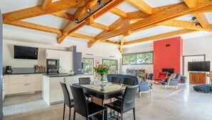 A modern kitchen with built-in appliances, a dining area with a glass-top table, and a red accent wall. - Appartement Exceptionnel de 230m2 Mansardé vue mer (La Ciotat)