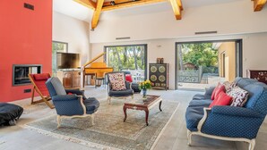 A spacious living room with a high ceiling, wooden beams, a piano, and a large window offering a view of the outdoors. - Appartement Exceptionnel de 230m2 Mansardé vue mer (La Ciotat)