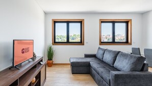 A modern living room with a grey sectional sofa, a wooden TV stand, and a potted plant. - GuestReady - Stunning Douro River Vista (Vila Nova de Gaia)