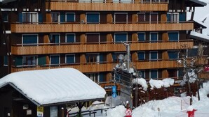 A multi-story hotel with wooden balconies and a ski lift visible in the background.