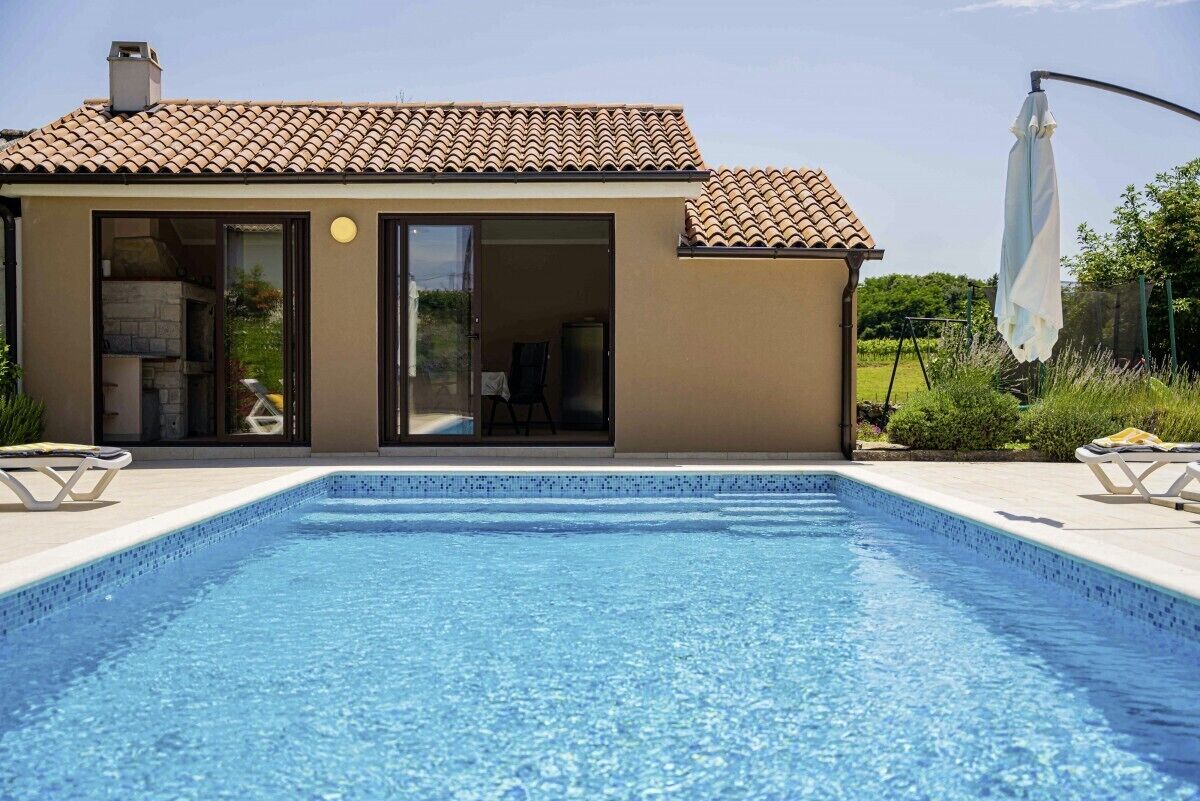 Une maison moderne dotée d’une piscine, d’un patio avec des chaises longues et d’un jardin.