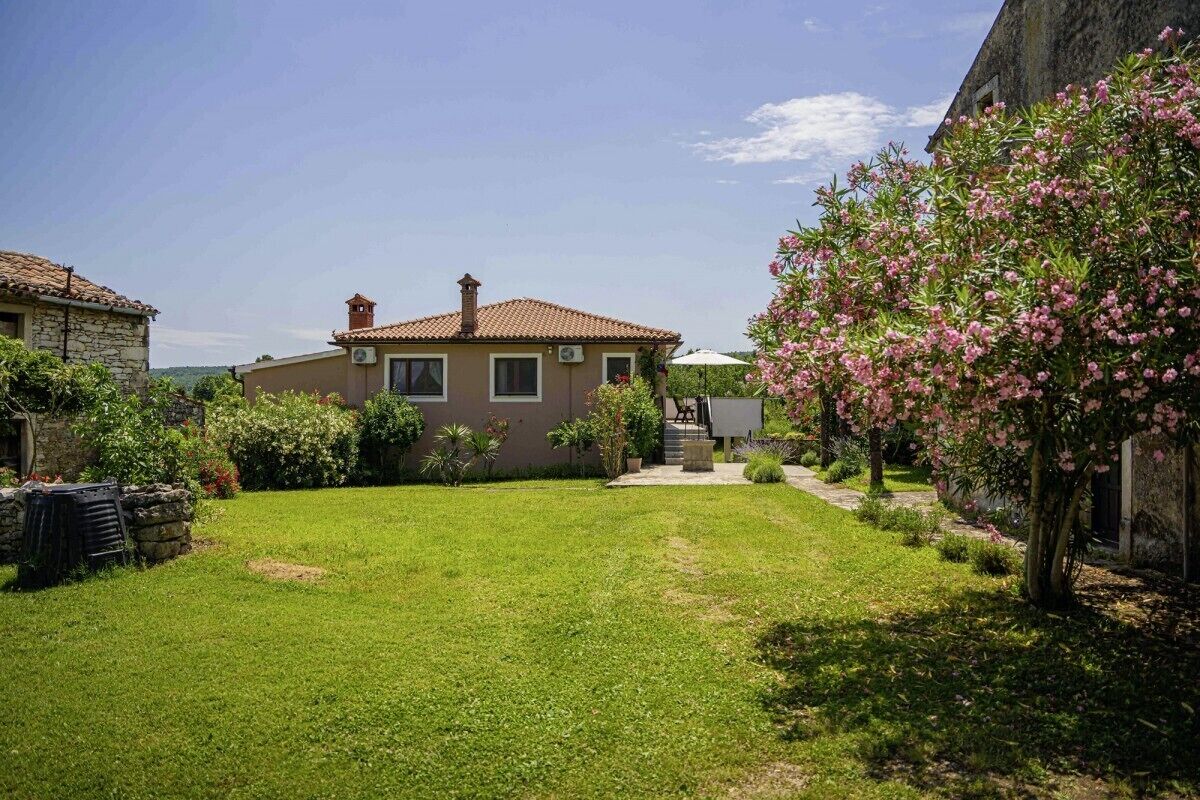 Uma casa com jardim, um muro de pedra e uma árvore florida em tons de rosa.