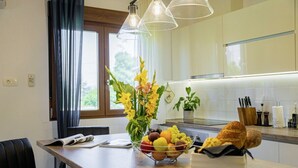 A modern kitchen with a wooden countertop, a fruit bowl, a vase with flowers, and a bread basket.