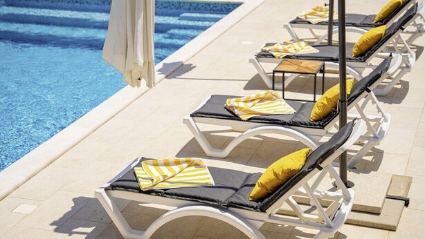 A poolside area with sun loungers, each with a cushion and a towel.