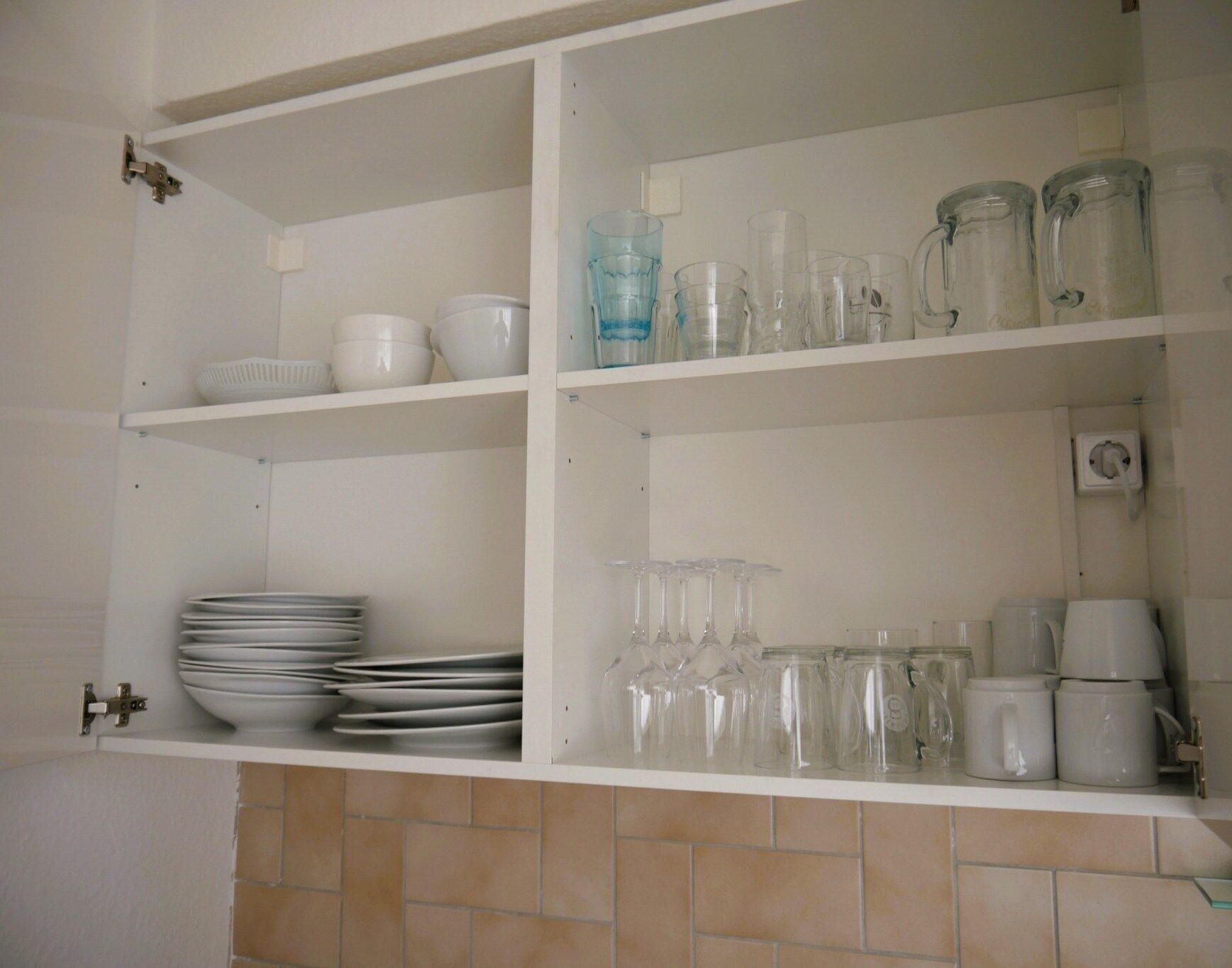 A kitchen with white cabinets, a tiled backsplash, and shelves holding white bowls, plates, and glassware.