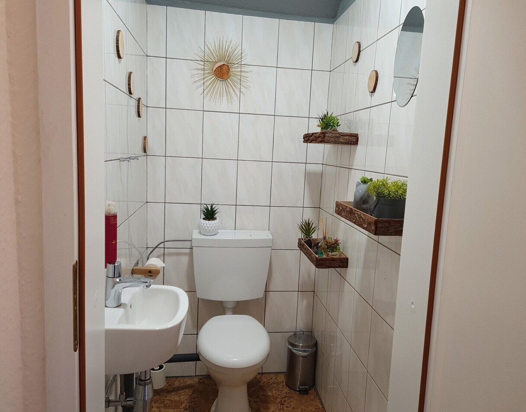 Une petite salle de bain comprenant des toilettes, un lavabo et deux étagères murales ornées de plantes.