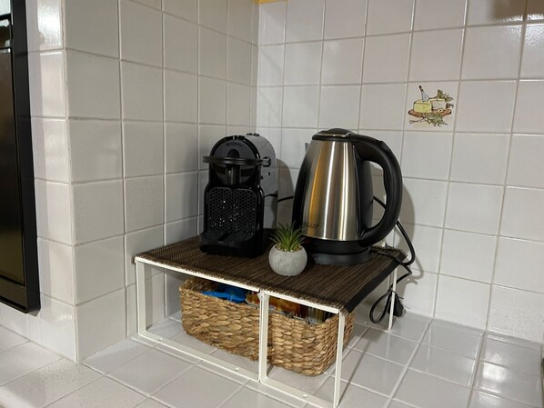 A kitchen counter with a coffee maker, a kettle, and a small potted plant.