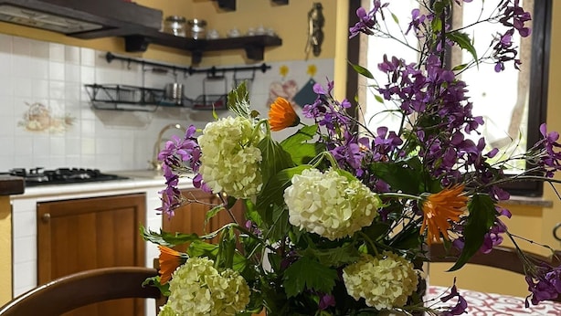 Een keuken met een eettafel, een bloemenvaas en een klok aan de muur.