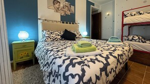 Een slaapkamer met een bed met een bedsprei, een nachtkastje met een lamp, een kunstwerk aan de muur en een stapelbed in de hoek.
