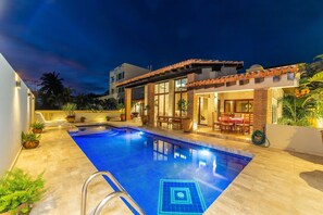 A swimming pool with a tiled deck, a covered patio area with a table and chairs, and a brick wall. - Casa Oaxaca with private pool (Bucerías)